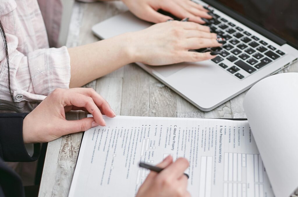 Two individuals working together on a home loan application, with one person typing on a laptop and the other reviewing and filling out forms on paper